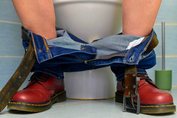 A man sitting on the toilet. A concept from the 1980s. Red punk shoes and jeans. Gender theme and urban culture. Punk subculture and nightlife in the city. stock photo