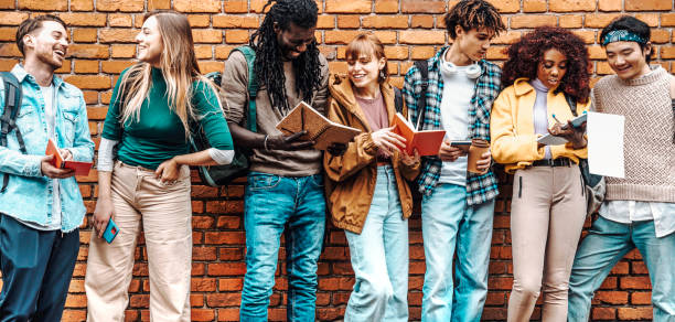 istock Happy young university students study with books leaning the wall out the campus - Group of youth multiracial people showing test results outside college - Multiethnic friends doing homework in school 1484104096