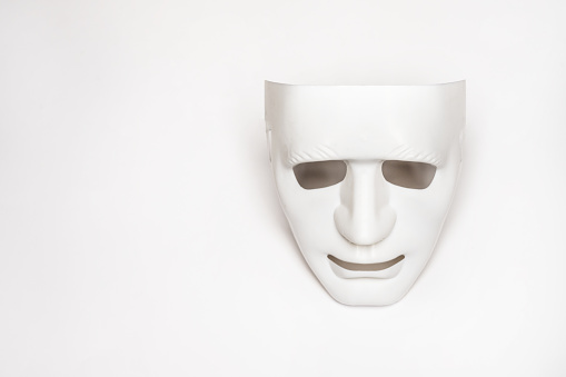 An expressionless white masquerade mask lying on a smooth white surface