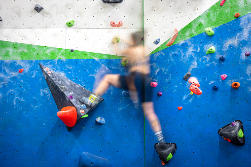 Detail of a vertical wall of an indoor climbing wall with holds of different colors to practice climbing with a blurred person climbing