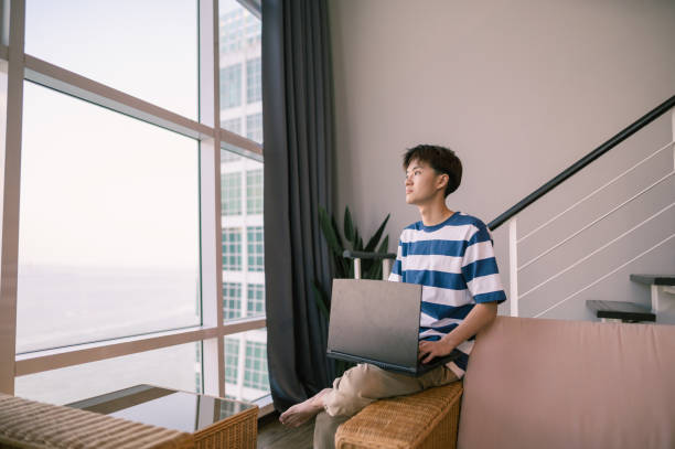 istock An Asian Chinese boy looking outside while using laptop in living room 1484114192