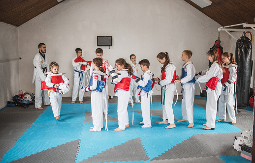 A group of children, dressed in kimonos, practice taekwondo together, led by a martial arts coach
