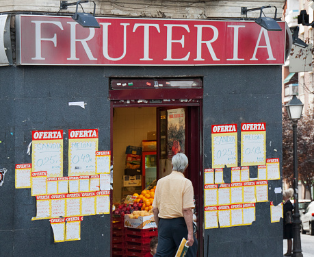 Madrid, Spain_ September 21, 2010:  groceries store , doorway. Greengrocer commercial sign in spanish language. Fruit store, retail display, senior man walking by.