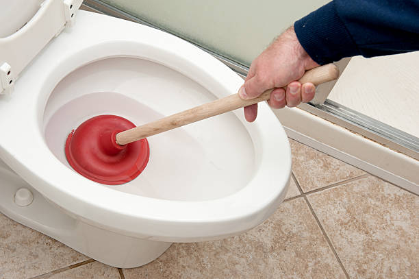 Plumber uncloging toilet A plumber uses a plunger to unclog a toilet. clogged stock pictures, royalty-free photos & images