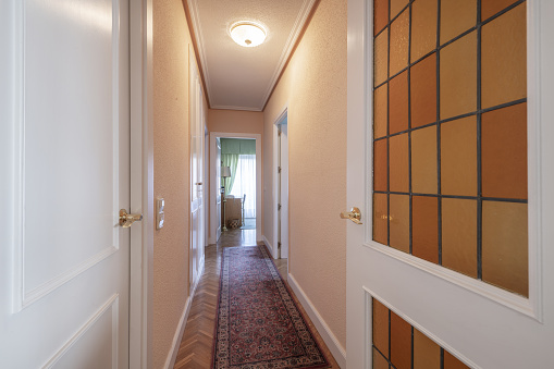 Distributor corridor of an urban residential house with white woodwork with leaded windows and parquet floors with narrow rugs throughout