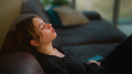 A young woman is relaxing on a sofa with her eyes closed.