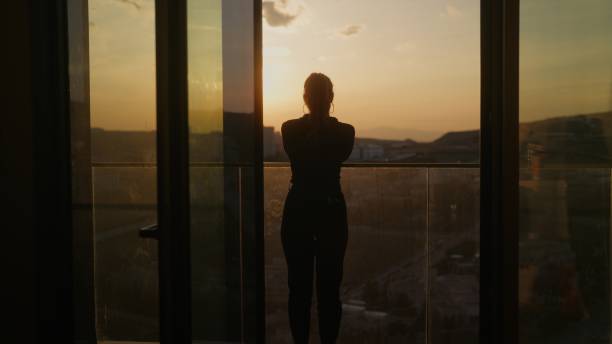 A young woman is standing at the balcony and watching the sunset.