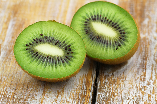 Closeup of two halves of juicy fresh kiwi fruit on rustic wooden surface