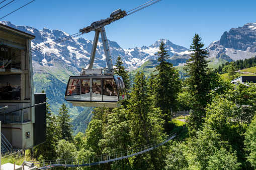 Murren, Switzerland - July 2, 2022: The overhead cablecar leaving Murren station taking hikers and tourists to the top of Schilthorn skyline view of Eiger, Monch and Jungfrau.