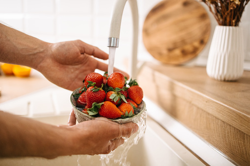Male hands holding a bowl with strawberries and washing them with clean water