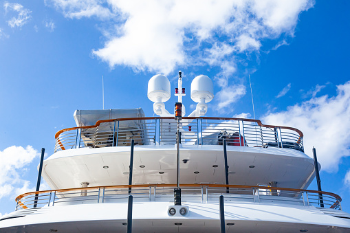 The stern of a luxury yacht with stainless steel railings and a mast at the top with radar, satellite equipment and mast lights.