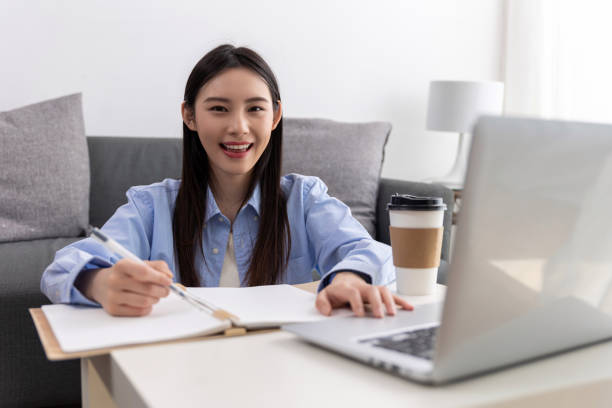 istock Beautiful young woman working on laptop computer while sitting at the living room, drinking coffee 1484145165