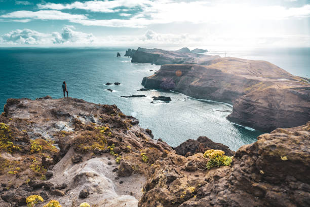 istock Backpacker woman enjoys panoramic view from a steep cliff overlooking the sea and the rugged foothills of Madeira's coast in the morning. Ponta do Bode, Madeira Island, Portugal, Europe. 1484146421
