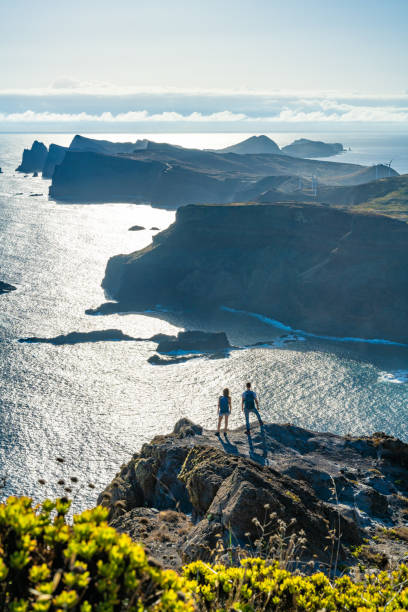 istock Backpacker couple enjoying the view from a vantage point on a steep cliff overlooking the sea and the rugged foothills of Madeira's coast in the morning. Ponta do Bode, Madeira Island, Portugal, Europe. 1484146827