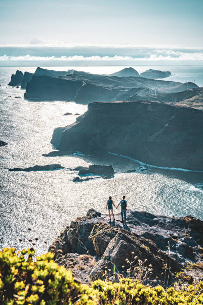 istock Backpacker couple enjoying the view from a vantage point on a steep cliff overlooking the sea and the rugged foothills of Madeira's coast in the morning. Ponta do Bode, Madeira Island, Portugal, Europe. 1484146847