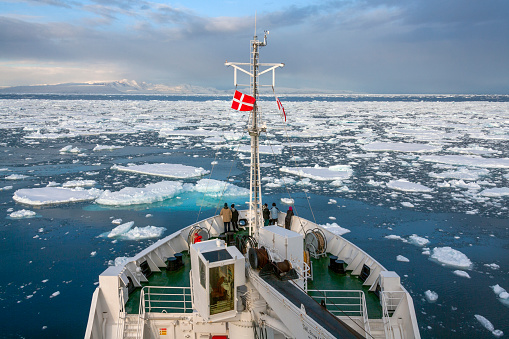 Adventure tourists on the bow of an icebreaker looking at the sea ice in the North Atlantic Ocean off the northeast coast of Greenland.