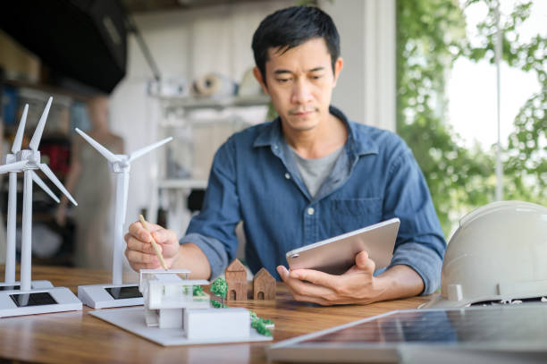 istock Selective focus on a pencil, Engineer sits holding tablet and looking at model of a house. with solar panels and model house on the table. To design use of renewable energy with wind and solar energy. 1484149214