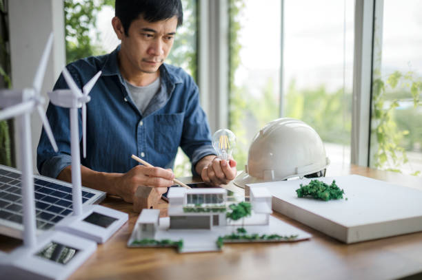 istock An engineer sits holding a light bulb and a tablet looking at a model of a house. with solar panels and a model house on the table. To design use of renewable energy with wind and solar energy. 1484149216