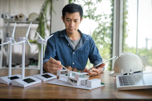 istock Selective focus on a pencil, Engineer sits holding tablet and looking at model of a house. with solar panels and model house on the table. To design use of renewable energy with wind and solar energy. 1484149218