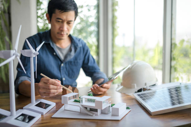 istock Selective focus on a pencil, Engineer sits holding tablet and looking at model of a house. with solar panels and model house on the table. To design use of renewable energy with wind and solar energy. 1484149219