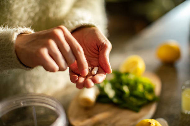 mujer joven tomando un suplemento de salud en la cocina - nutritional supplement fotografías e imágenes de stock