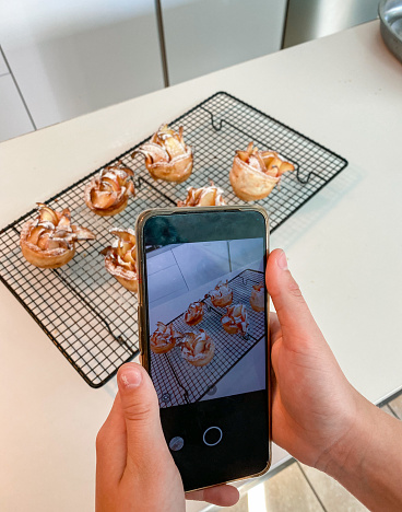 Hand holding mobile phone taking photo of rose shaped puff pastry apples ready to eat