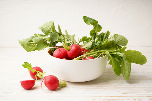 Ripe red radish in a bowl on a wooden background. Fresh red radish.