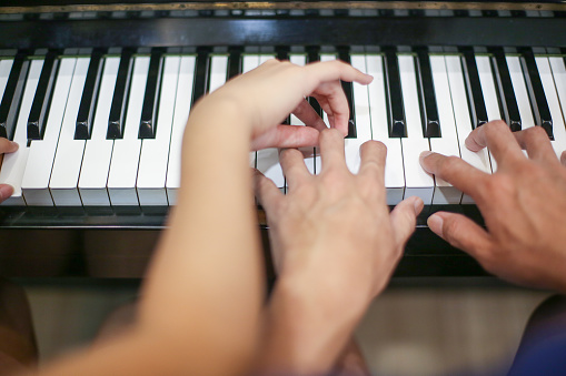 Human hand - An Asian young woman is guiding an Asian man on piano skills.