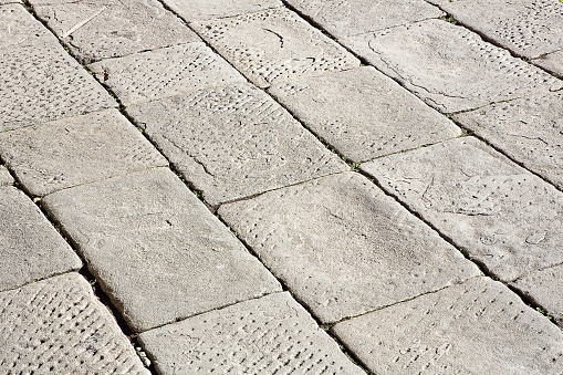 Old and damaged italian paving made with chiseled grey sandstone blocks in a pedestrian zone