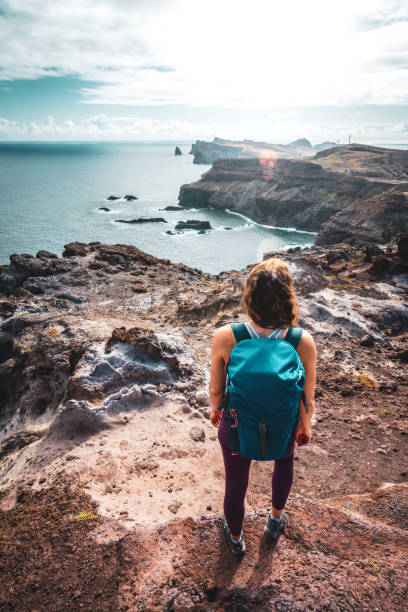 istock Backpacker woman enjoys panoramic view from a steep cliff overlooking the sea and the rugged foothills of Madeira's coast in the morning. Ponta do Bode, Madeira Island, Portugal, Europe. 1484158708