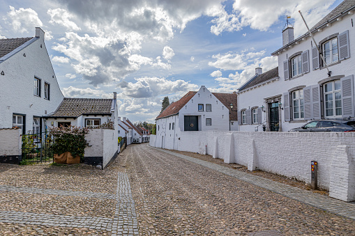 Architectural landscape of the white Dutch town of Thorn against blue cloud-capped sky, cobbled streets, houses with white walls, tiled gabled roofs, sunny day in Midden-Limburg in the Netherlands