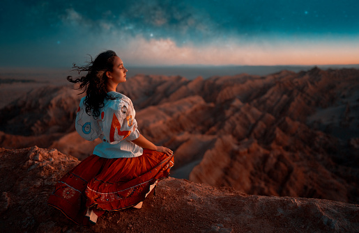 young woman sitting in viewpoint meditating breathing the warm breeze of the desert in San Pedro de Atacama