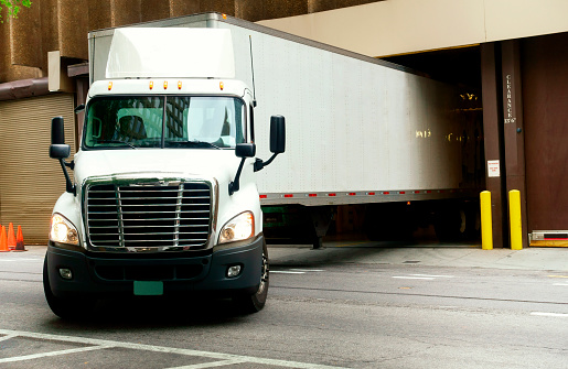 The semi truck with box trailer leaves the gate of multi story building after unloading the delivered cargo. Atlanta, Georgia, USA.