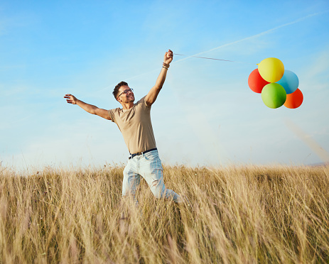 Happy young man running playing with balloons outdoors