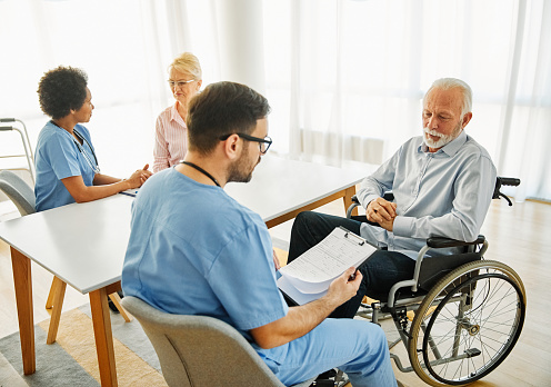 Doctor or nurse caregiver with senior man in a wheelchair  holding  a document paperwork at home or nursing home