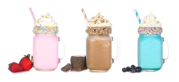 Fun colorful summer milkshakes in mason jar glasses isolated on a white background. Strawberry, chocolate and blueberry sweet drinks with ingredients.