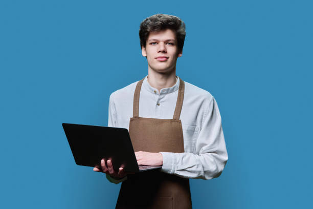 istock Young male in an apron with laptop, on blue background 1484169510