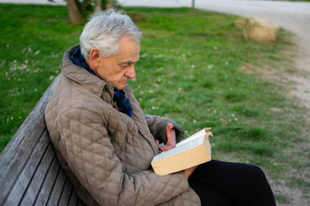 istock Old man with gray hair reading a book sited on an bench. 1484170484
