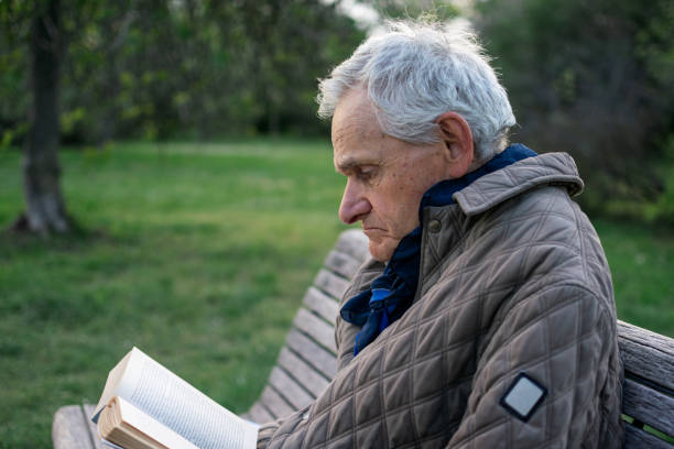 istock Old man with gray hair reading a book sited on an bench. 1484170522