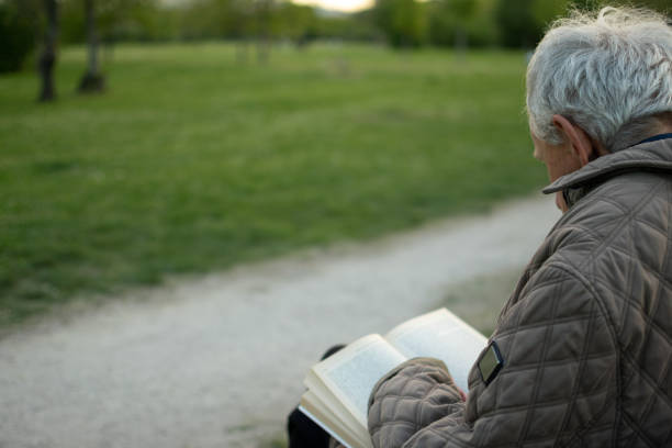 istock Old man with gray hair reading a book sited on an bench. 1484170664