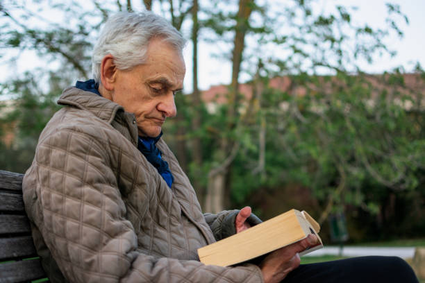 istock Old man with gray hair reading a book sited on an bench. 1484170681
