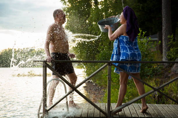 pareja de ancianos divirtiéndose después de la sauna finlandesa en el muelle de la cabaña de madera en un lago - finland lake summer couple fotografías e imágenes de stock