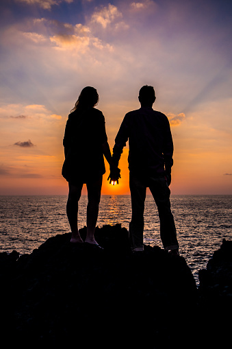 Couple In Love Holding Hands During a Classic Sunset. Golden Hour. Contrast Clouds Ocean. Silhouette