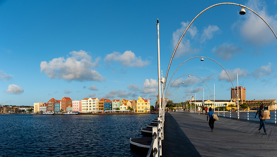 Passerby on the Queen Emma Bridge with classical architecture buildings in the background in the city of Willemstad. Curaçao. Netherlands Antilles. July 26, 2022.