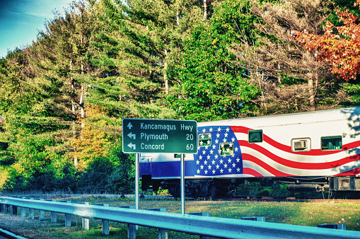 Big truck with american flag along a road in foliage season.