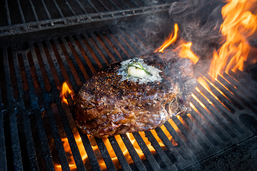 Roasted beef ripe steaks on flaming charcoal grill with blurred background of camping area in natural parkland
