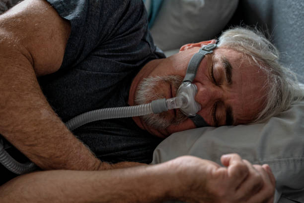 istock A 60-year-old man sleeps with a CPAP machine in bed. The machine helps him breathe easier by delivering continuous positive airway pressure, improving his sleep quality and overall health. 1484190957