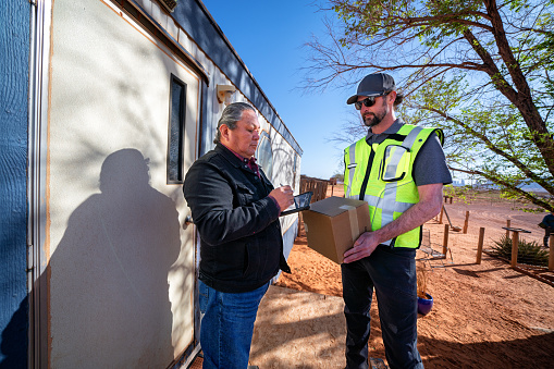 A man delivers a package to an elderly indigenous Navajo man at a modular home in Monument Valley, Utah. The small town is known for its breathtaking natural landscapes