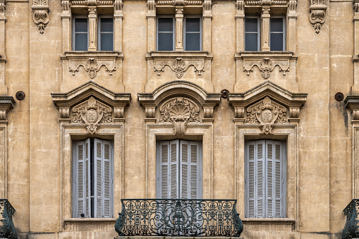 Beautiful old Parisian residential building, with traditional full length windows and exterior ornate wrought iron railings. The main entrance has an elegant, wooden door.