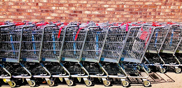 A sideview image of a row of metal shopping carts in front of the exterior red brick building of a grocery store in Hoboken, New Jersey.